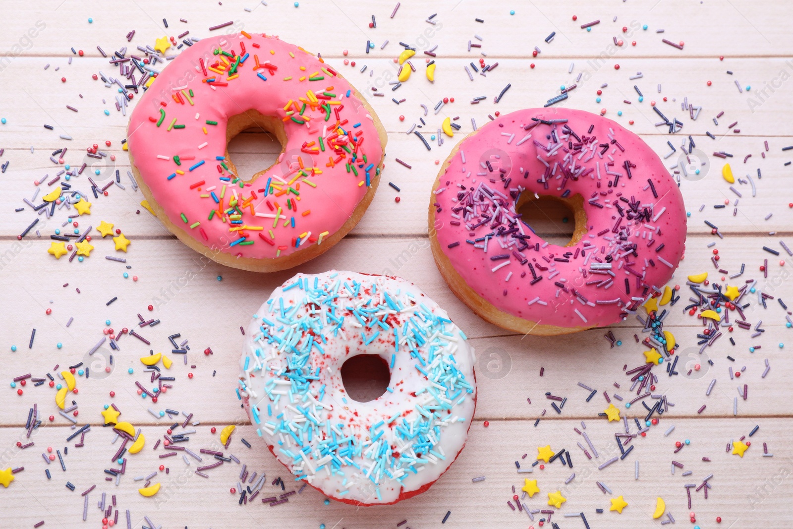 Photo of Glazed donuts decorated with sprinkles on white wooden table, flat lay. Tasty confectionery