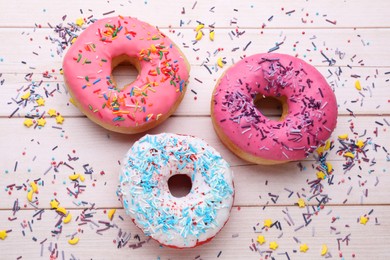 Photo of Glazed donuts decorated with sprinkles on white wooden table, flat lay. Tasty confectionery
