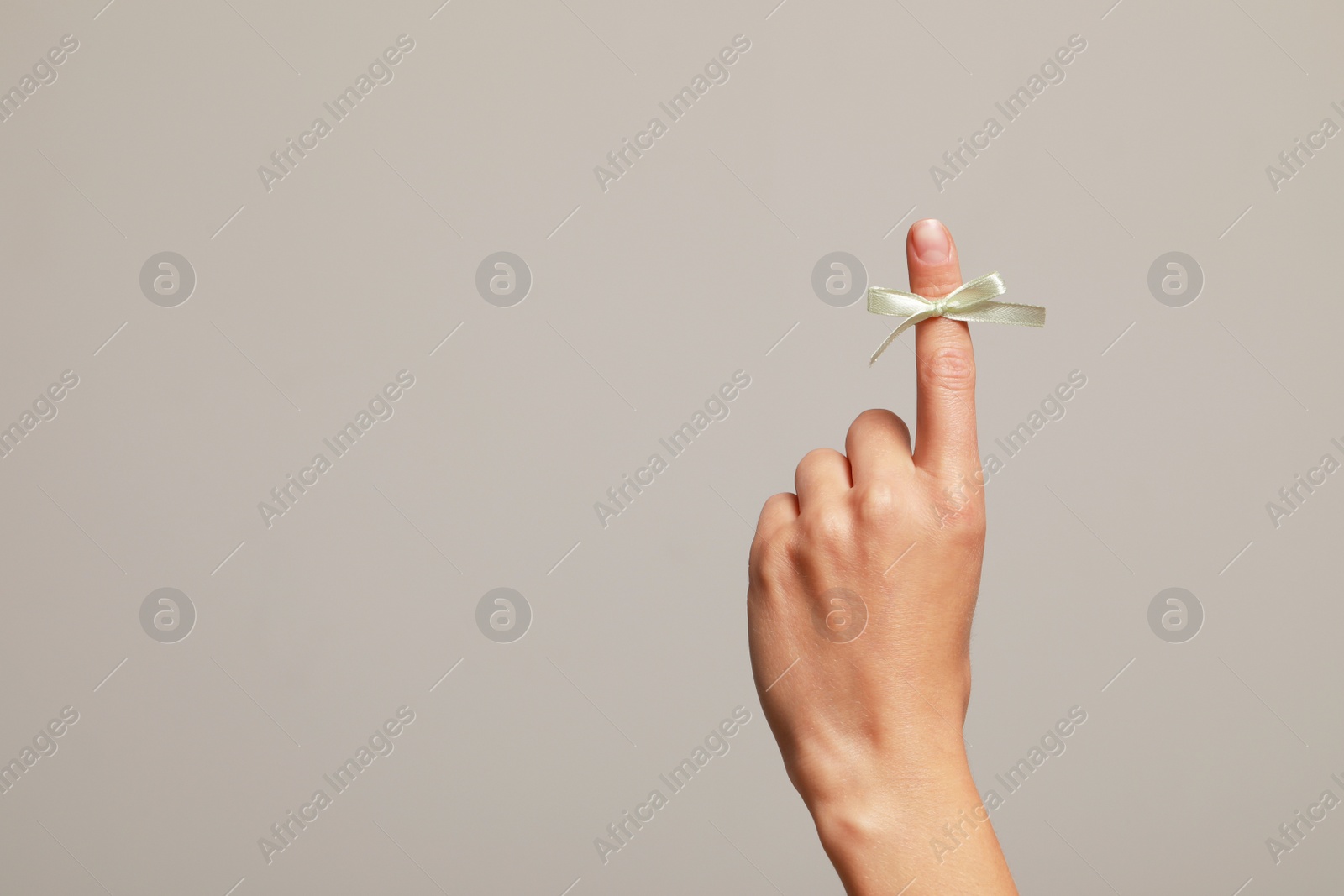 Photo of Woman showing index finger with tied bow as reminder on grey background, closeup. Space for text