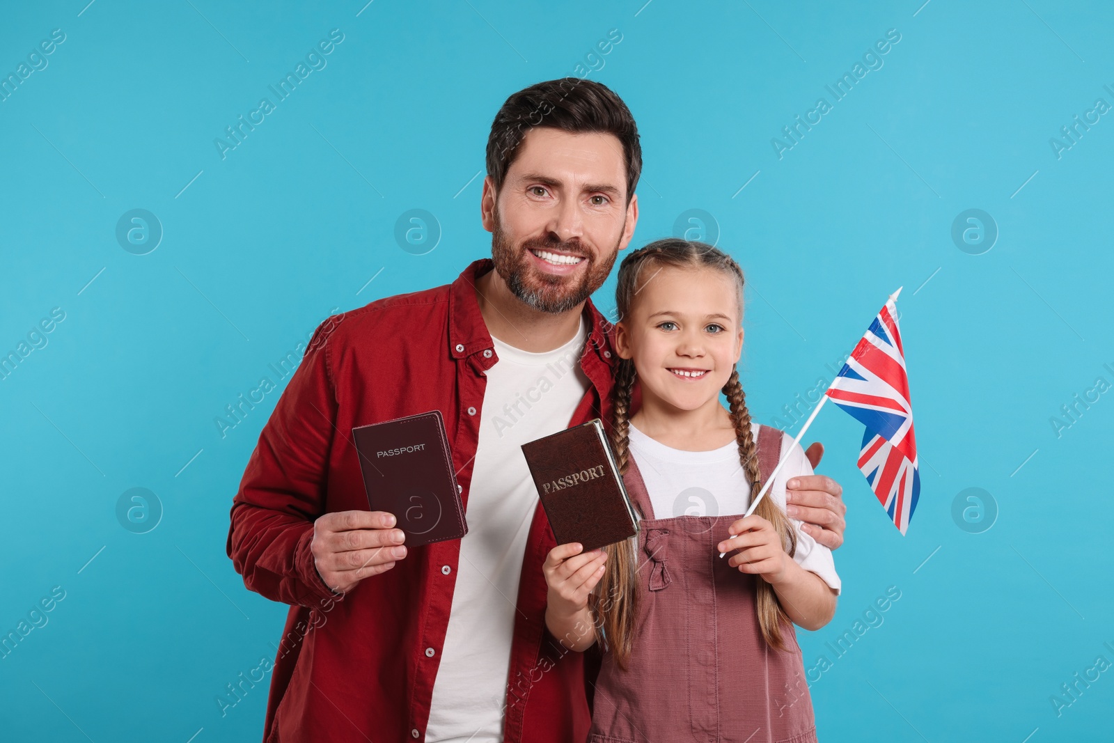 Photo of Immigration. Happy man with his daughter holding passports and flag of United Kingdom on light blue background, space for text