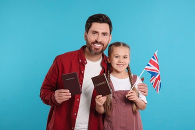 Photo of Immigration. Happy man with his daughter holding passports and flag of United Kingdom on light blue background, space for text