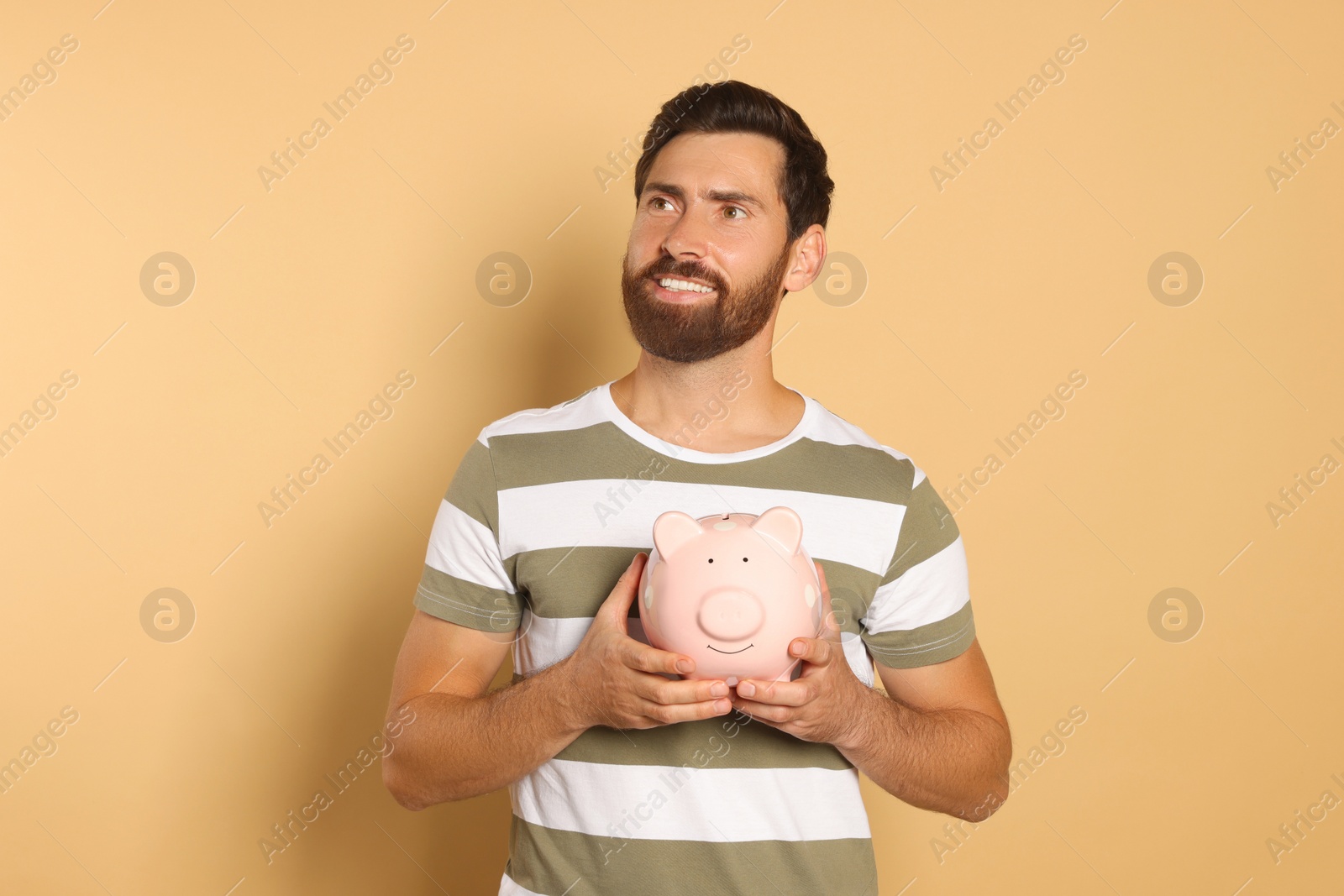 Photo of Happy man with ceramic piggy bank on beige background