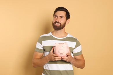 Happy man with ceramic piggy bank on beige background