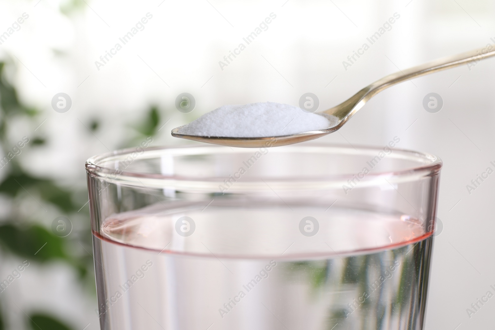 Photo of Spoon with baking soda over glass of water on blurred background, closeup