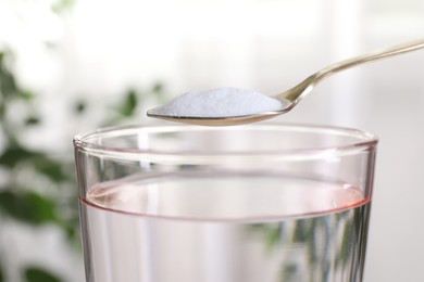 Photo of Spoon with baking soda over glass of water on blurred background, closeup