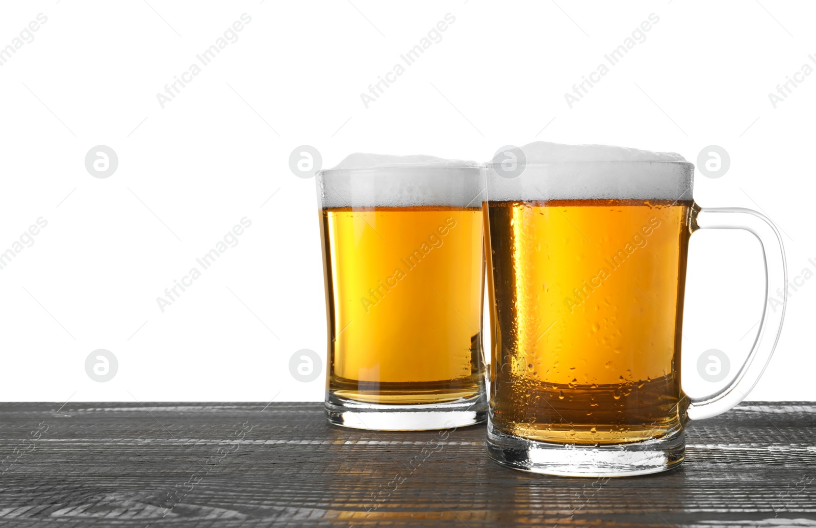 Photo of Glass mugs of tasty beer on grey wooden table against white background