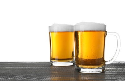 Photo of Glass mugs of tasty beer on grey wooden table against white background