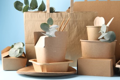 Photo of Eco friendly food packaging. Paper containers, tableware, bag and eucalyptus branches on white table against light blue background