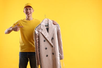 Dry-cleaning delivery. Happy courier holding coat in plastic bag on orange background, space for text