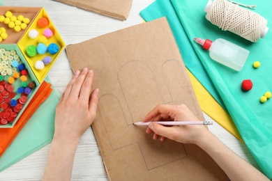 Woman drawing cactus on cardboard paper at white wooden table, top view. Pinata DIY