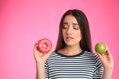 Woman choosing between apple and doughnut on pink background