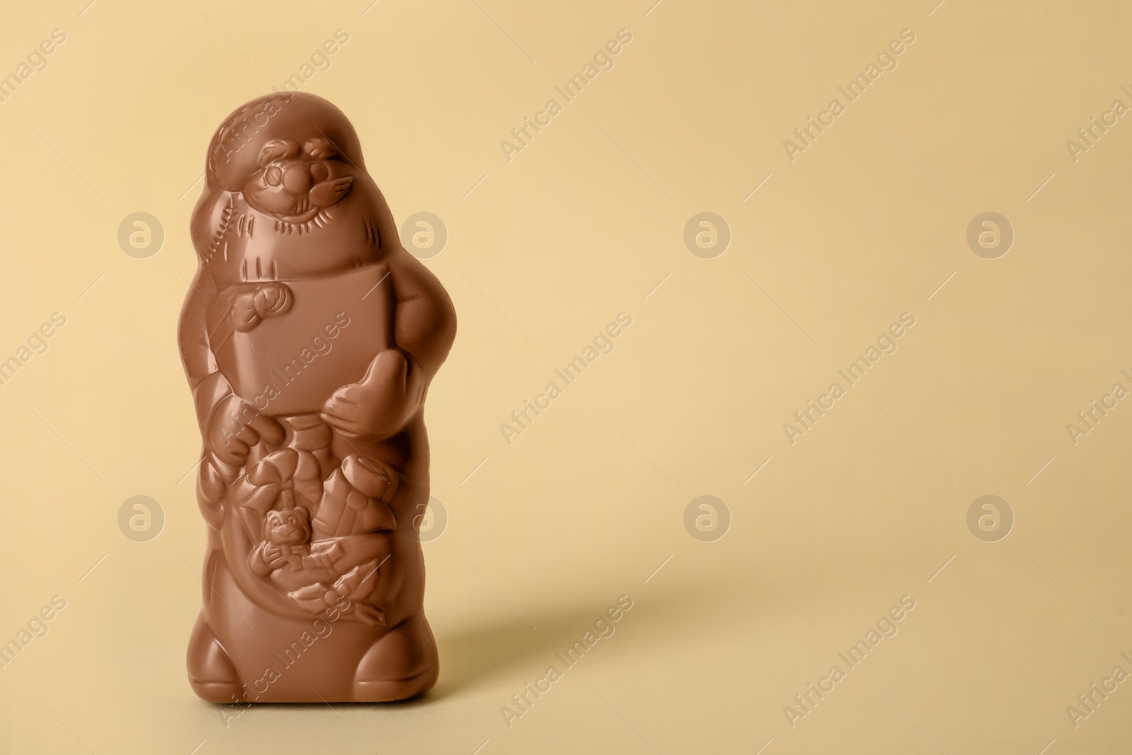 Photo of Unwrapped chocolate Santa Claus on beige background. Space for text