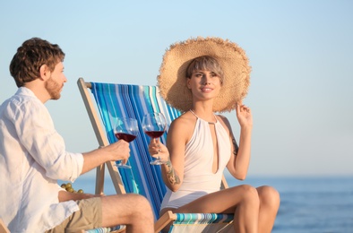 Photo of Young couple with glasses of wine in beach chairs at seacoast