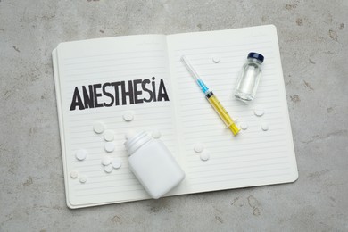 Notebook with word Anesthesia and different drugs on light table, top view