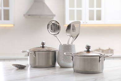 Photo of Stainless steel pots and kitchen utensils on white table indoors