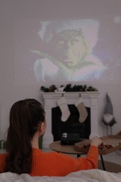 Lviv, Ukraine – January 24, 2023: Woman watching How the Grinch Stole Christmas movie via video projector at home, back view