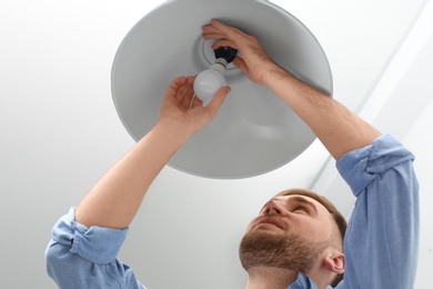 Photo of Man changing light bulb in lamp indoors