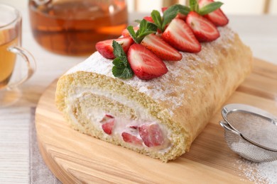 Delicious cake roll with strawberries and cream on wooden board, closeup