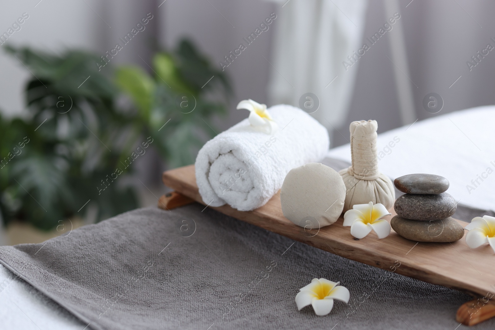 Photo of Stacked spa stones, flowers, herbal bags and towel on massage table indoors