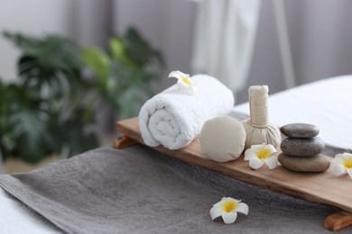 Stacked spa stones, flowers, herbal bags and towel on massage table indoors