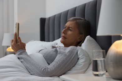 Photo of Menopause. Sleepless woman using smartphone in bed indoors