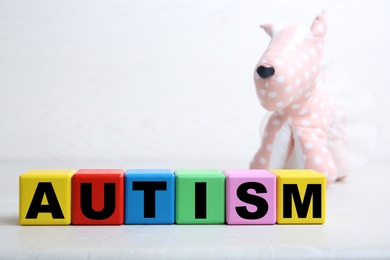 Colorful cubes with word AUTISM and toy dog on table against light background