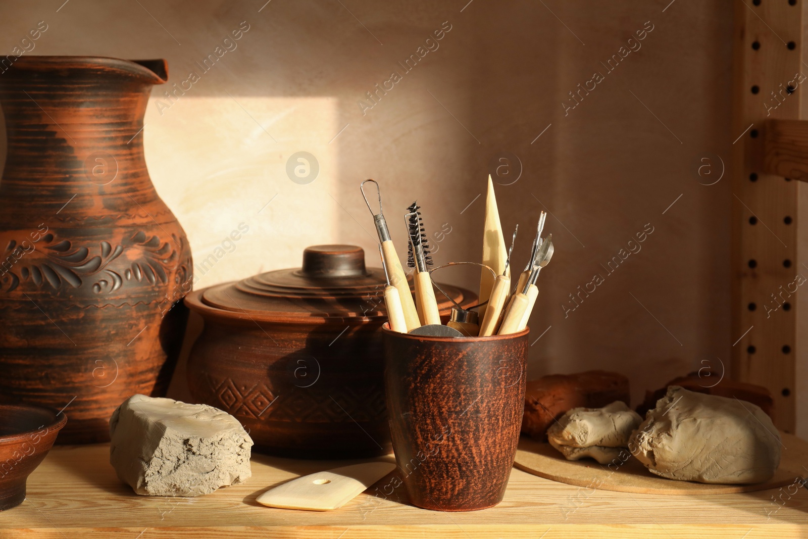 Photo of Set of different crafting tools and clay dishes on wooden rack in workshop