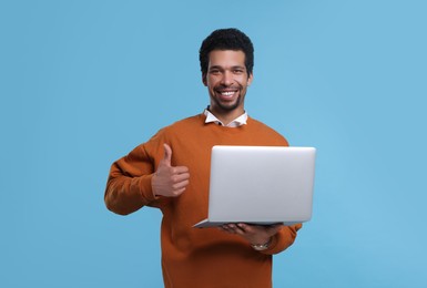 Photo of Happy man with laptop showing thumb up on light blue background