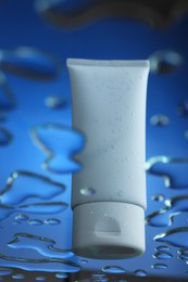 Photo of Moisturizing cream in tube on glass with water drops against blue background, low angle view