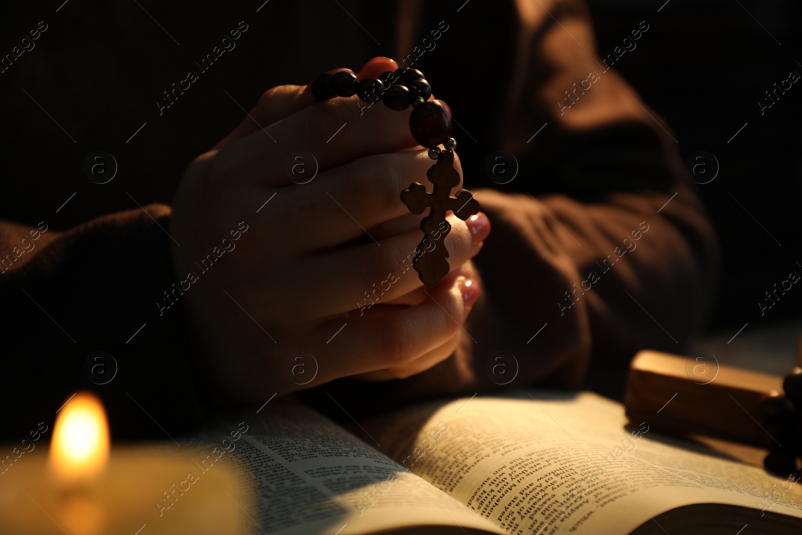 Photo of Woman praying at table with burning candle and Bible, closeup