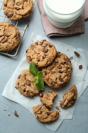 Photo of Tasty chocolate chip cookies, glass of milk and mint leaves on light grey table, flat lay