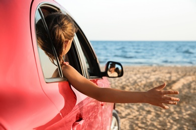 Little girl leaning out of car window on beach. Summer trip