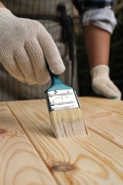 Man varnishing wooden surface with brush outdoors, closeup