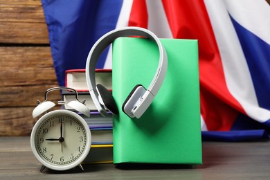 Photo of Learning foreign language. Different books, headphones and alarm clock on wooden table near flag of United Kingdom
