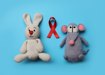 Photo of Cute knitted toys and red ribbon on blue background, flat lay. AIDS disease awareness