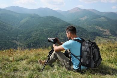 Professional photographer taking picture with modern camera in mountains. Space for text