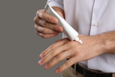 Photo of Man applying cream from tube onto hand on grey background, closeup