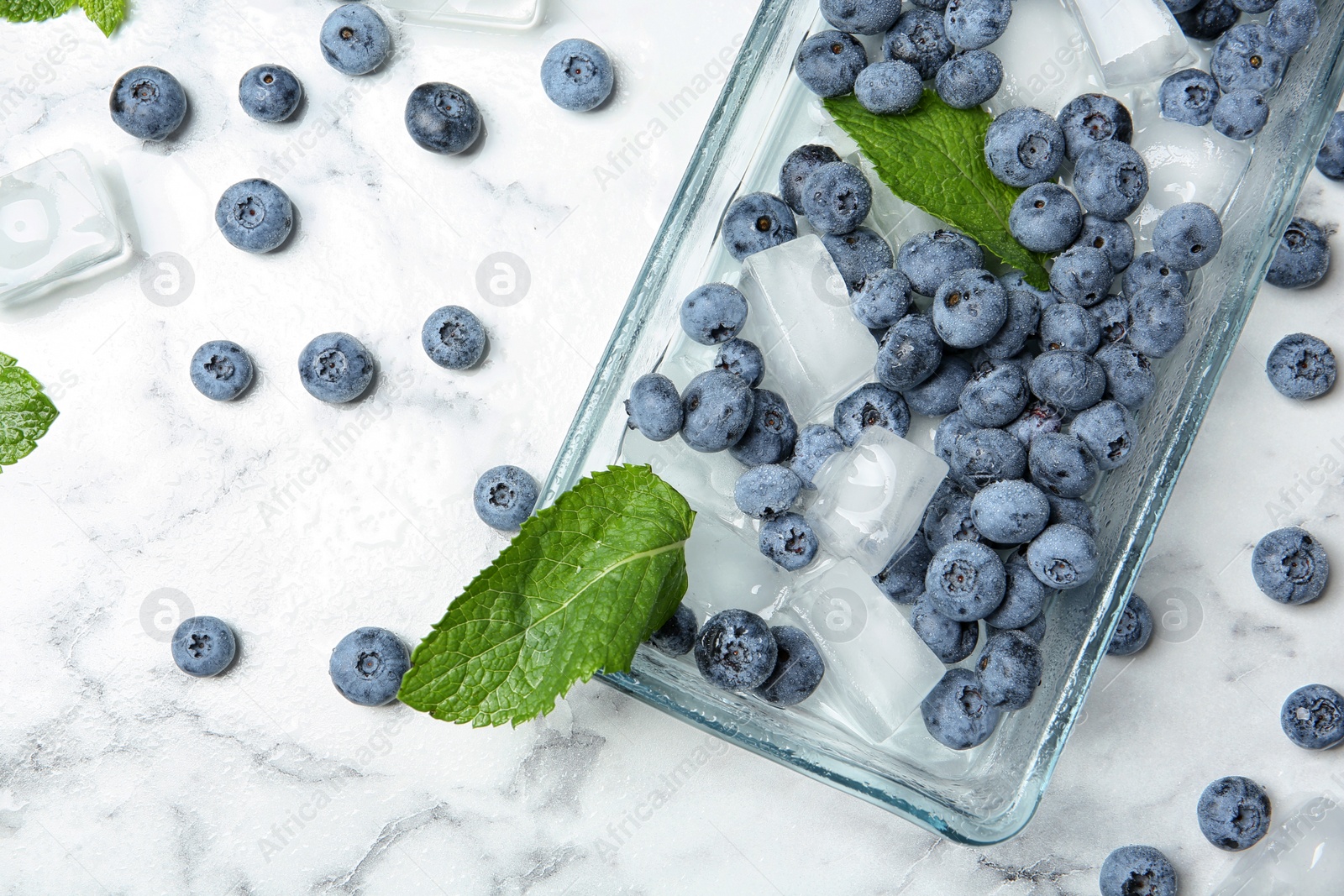 Photo of Flat lay composition with juicy blueberries, green leaves and ice on marble table