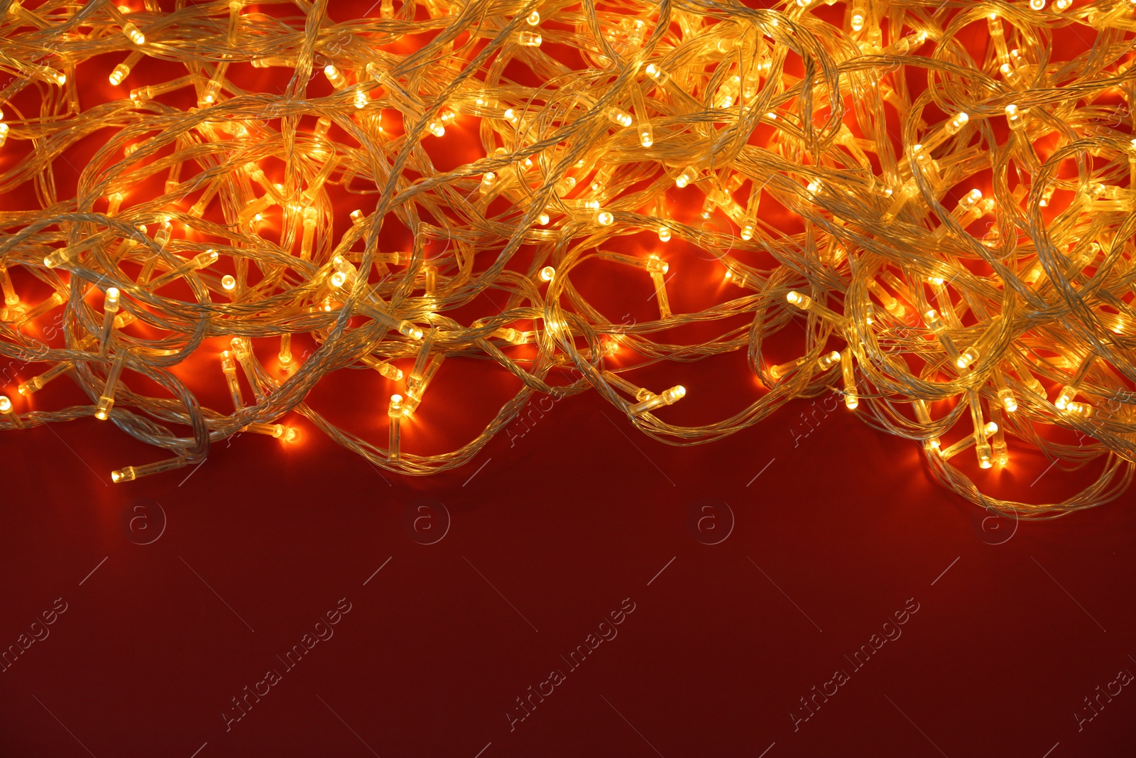 Photo of Glowing Christmas lights on red background, top view. Space for text