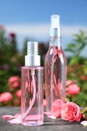 Photo of Bottles of facial toner with essential oil and fresh roses on table against blurred background