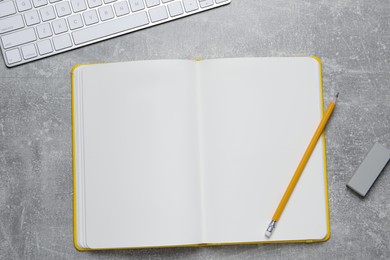 Photo of Open blank notebook, keyboard pencil and eraser on light grey table, flat lay