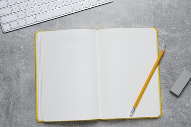 Open blank notebook, keyboard pencil and eraser on light grey table, flat lay