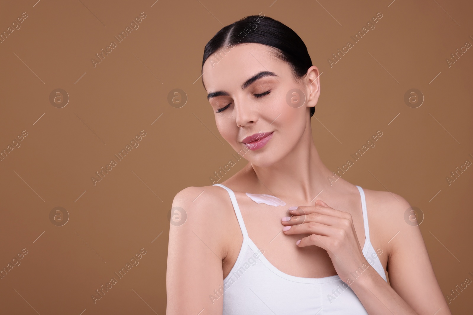 Photo of Beautiful woman with smear of body cream on her collarbone against light brown background. Space for text