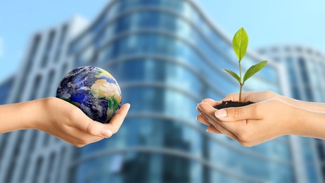 Image of Make Earth green. Women holding globe and seedling against blurred building, closeup