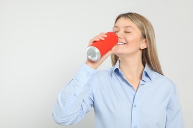 Beautiful happy woman drinking from red beverage can on light background. Space for text