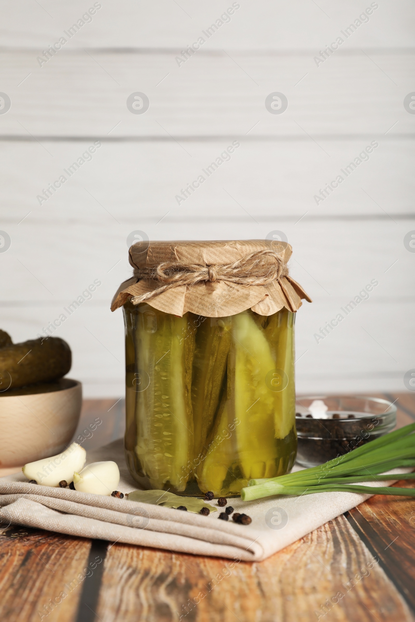 Photo of Jar of pickled cucumbers, fresh green onion, peppercorns and garlic on wooden table