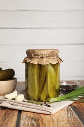 Jar of pickled cucumbers, fresh green onion, peppercorns and garlic on wooden table