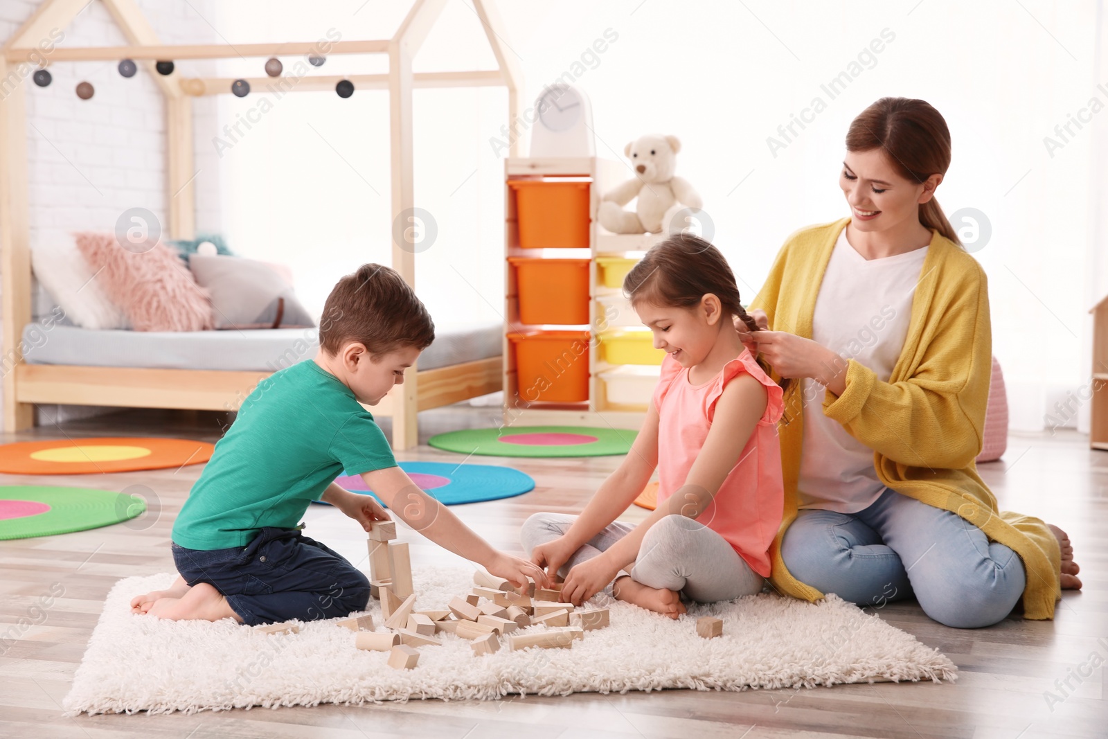 Photo of Little children playing while nanny braiding girl's hair at home