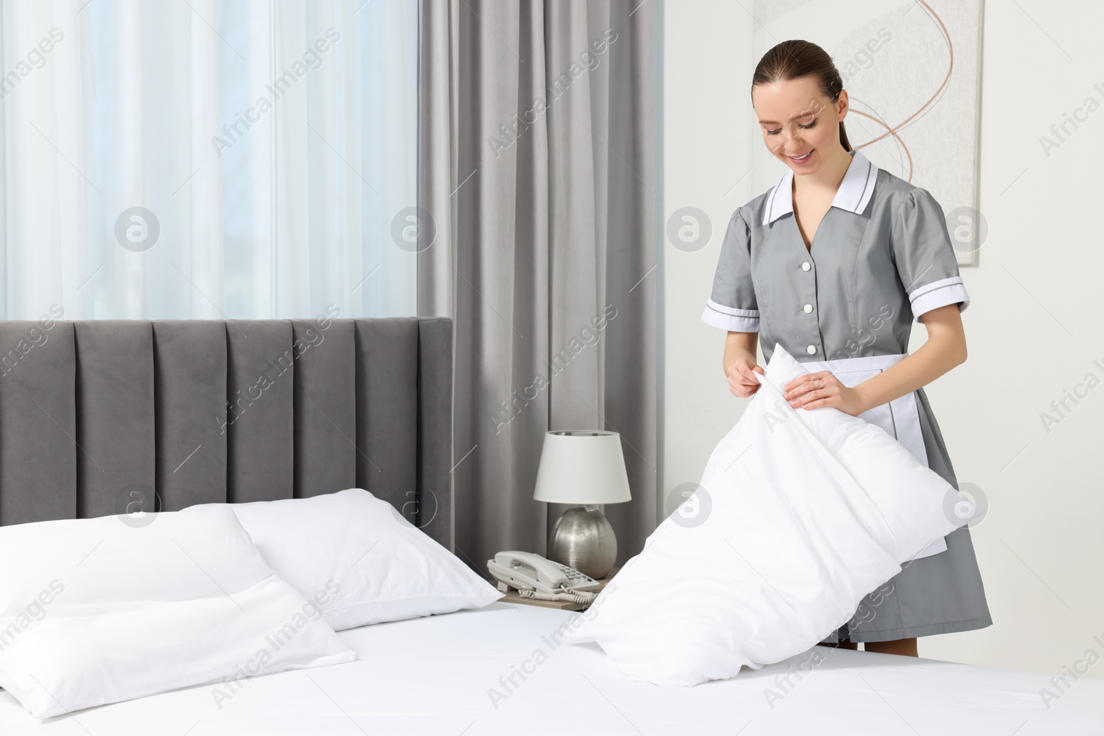 Photo of Young maid making bed in hotel room. Space for text