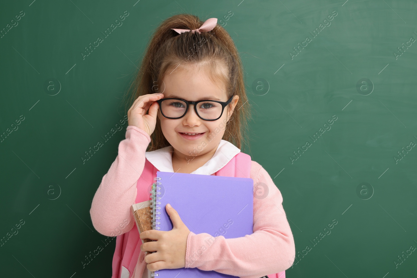 Photo of Happy little school child with notebooks near chalkboard